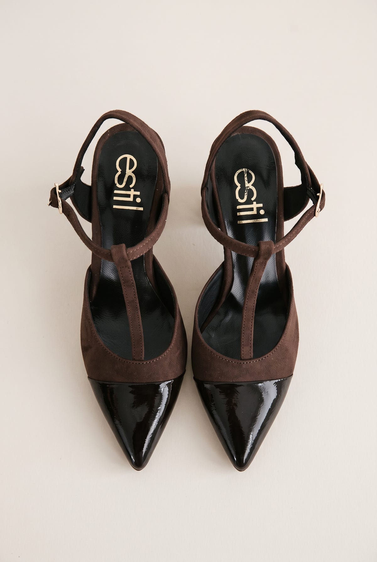 Top view of chocolate suede T-strap pumps with black patent pointed toes placed side by side