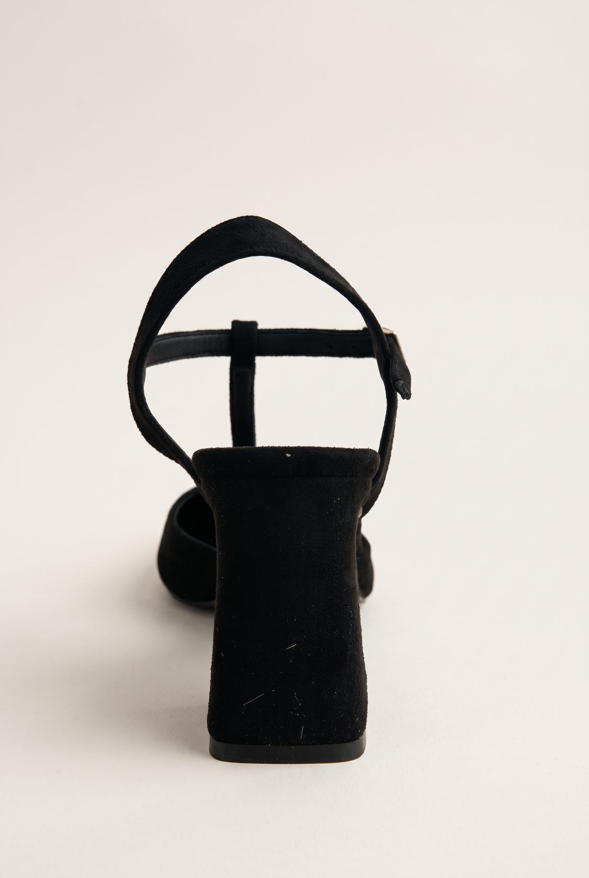 Rear view of black suede T-strap pump showing arched ankle strap and flared block heel