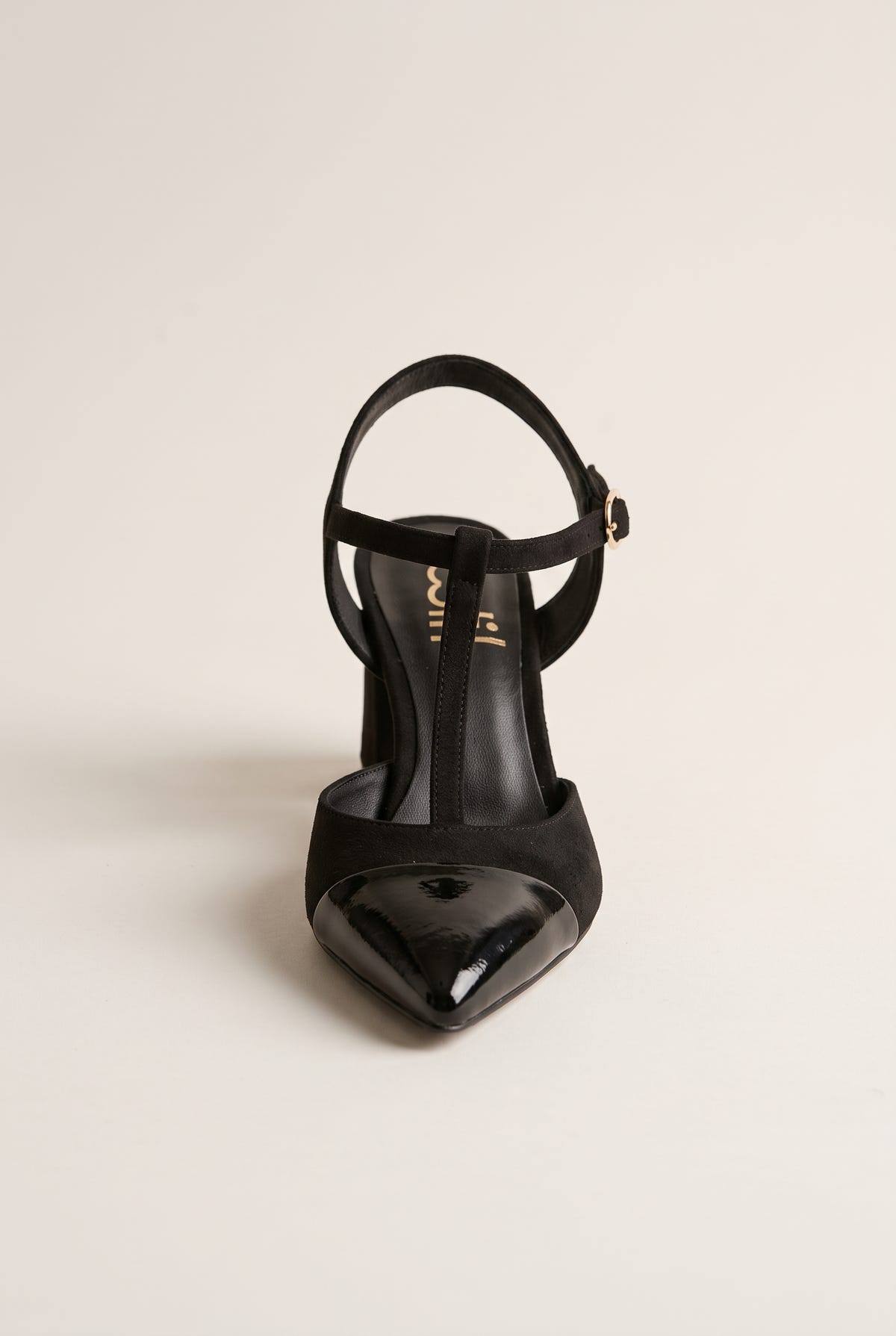 Front view of black suede T-strap pump showing patent toe cap and buckle on ankle strap