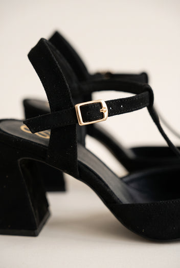 Close-up of black suede T-strap showing buckle, flared heel edge and suede texture