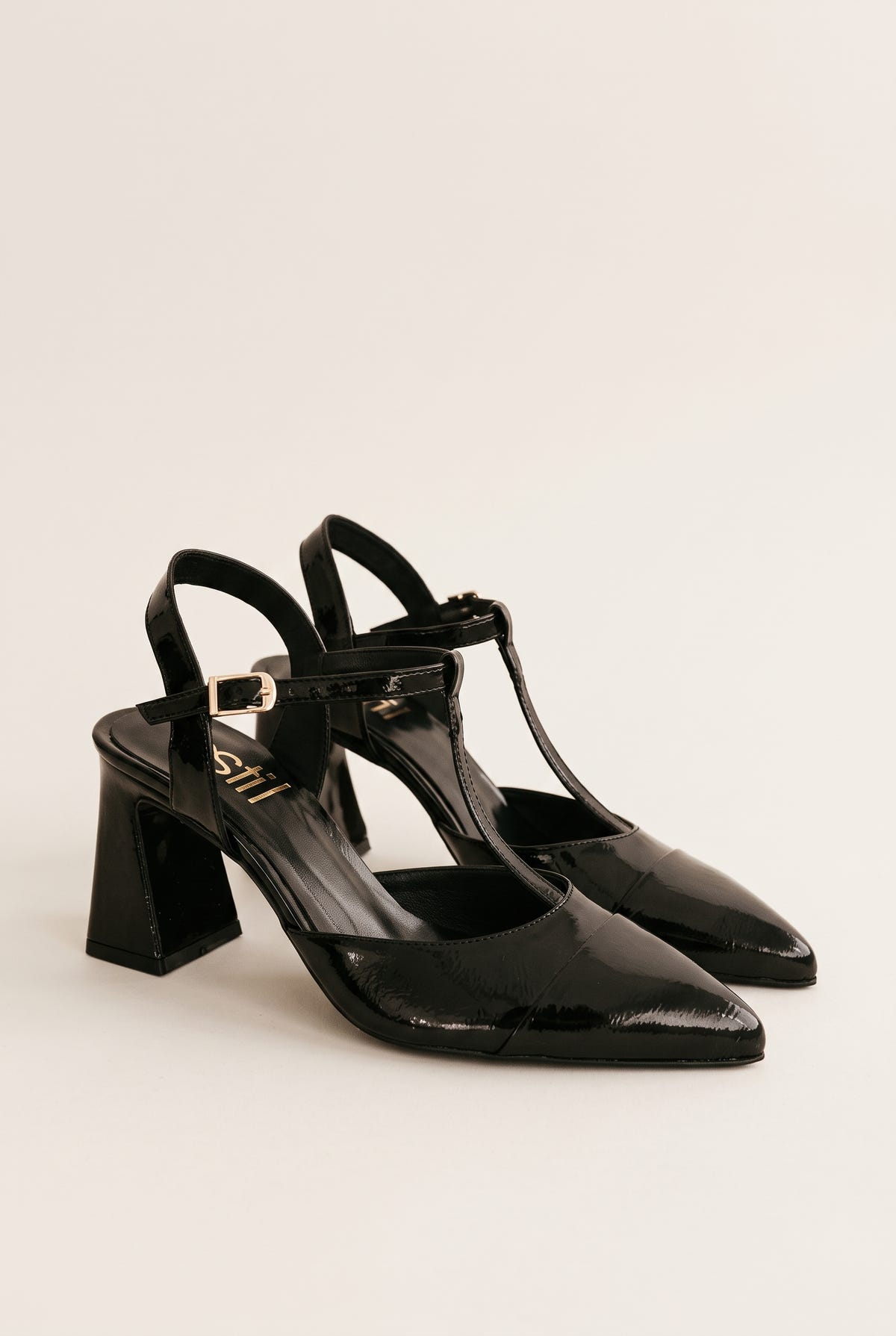 Pair of black patent T-strap pumps in angled view showing ankle straps and block heels