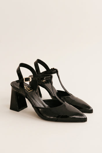Pair of black patent T-strap pumps in angled view showing ankle straps and block heels
