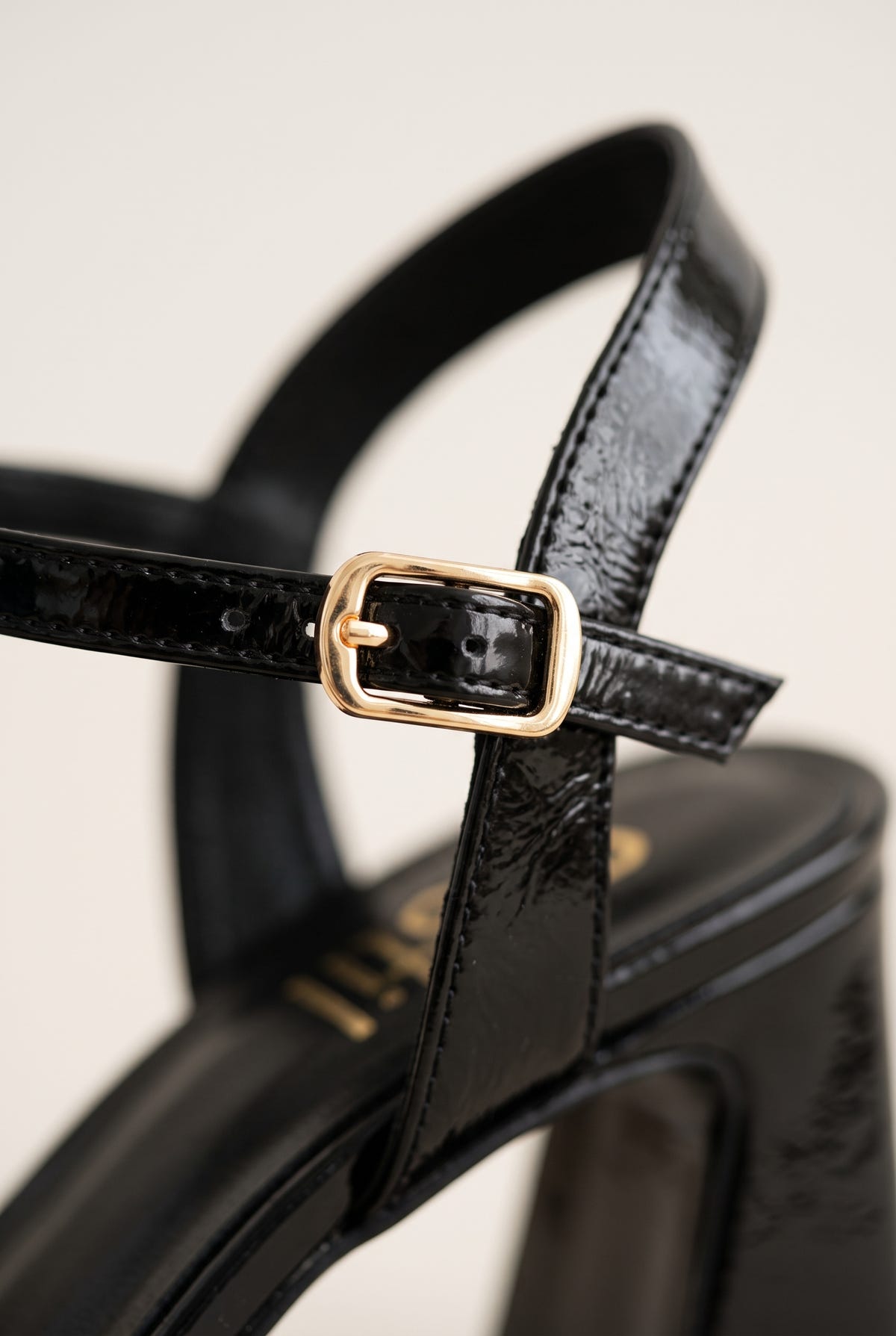 Close-up of black patent ankle strap showing gold-tone buckle and glossy leather finish