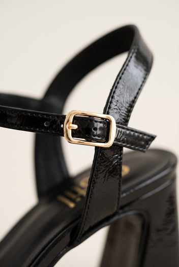 Close-up of black patent ankle strap showing gold-tone buckle and glossy leather finish
