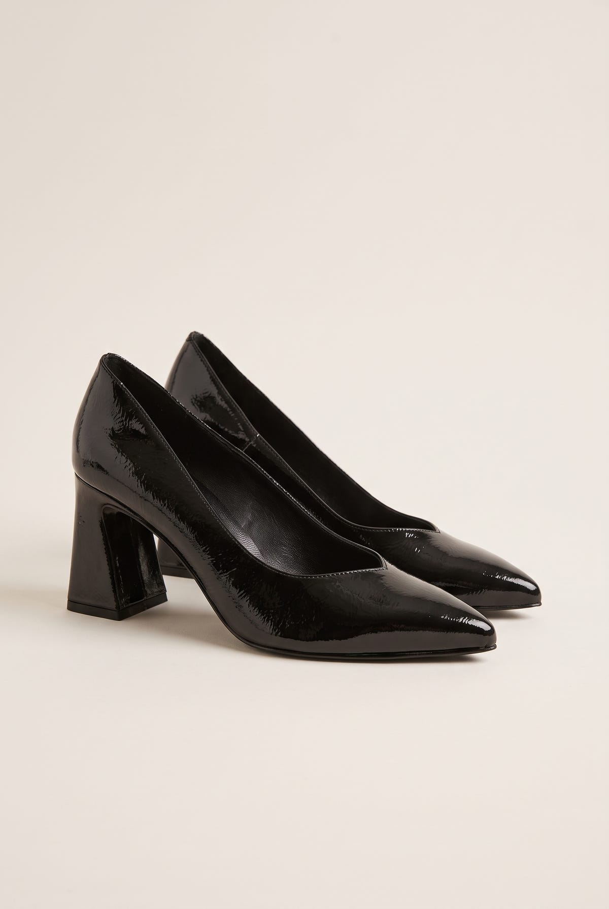 Pair of black patent pointed-toe pumps in three-quarter view showing flared block heels and glossy finish