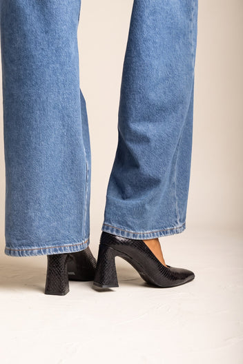 Black snake-embossed pumps with block heel and pointed toe, front view of both feet in wide-leg jeans