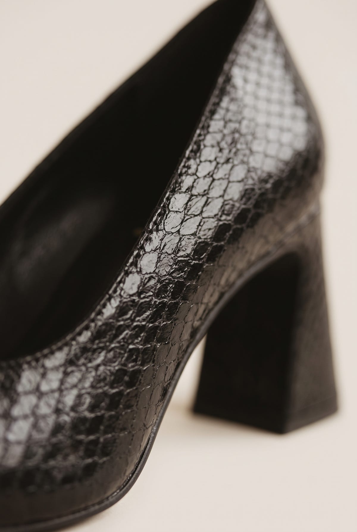 Close-up of black snake-embossed leather showing scale texture along the flared block heel