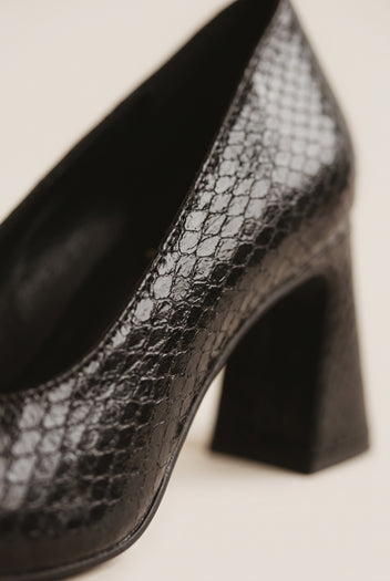 Close-up of black snake-embossed leather showing scale texture along the flared block heel