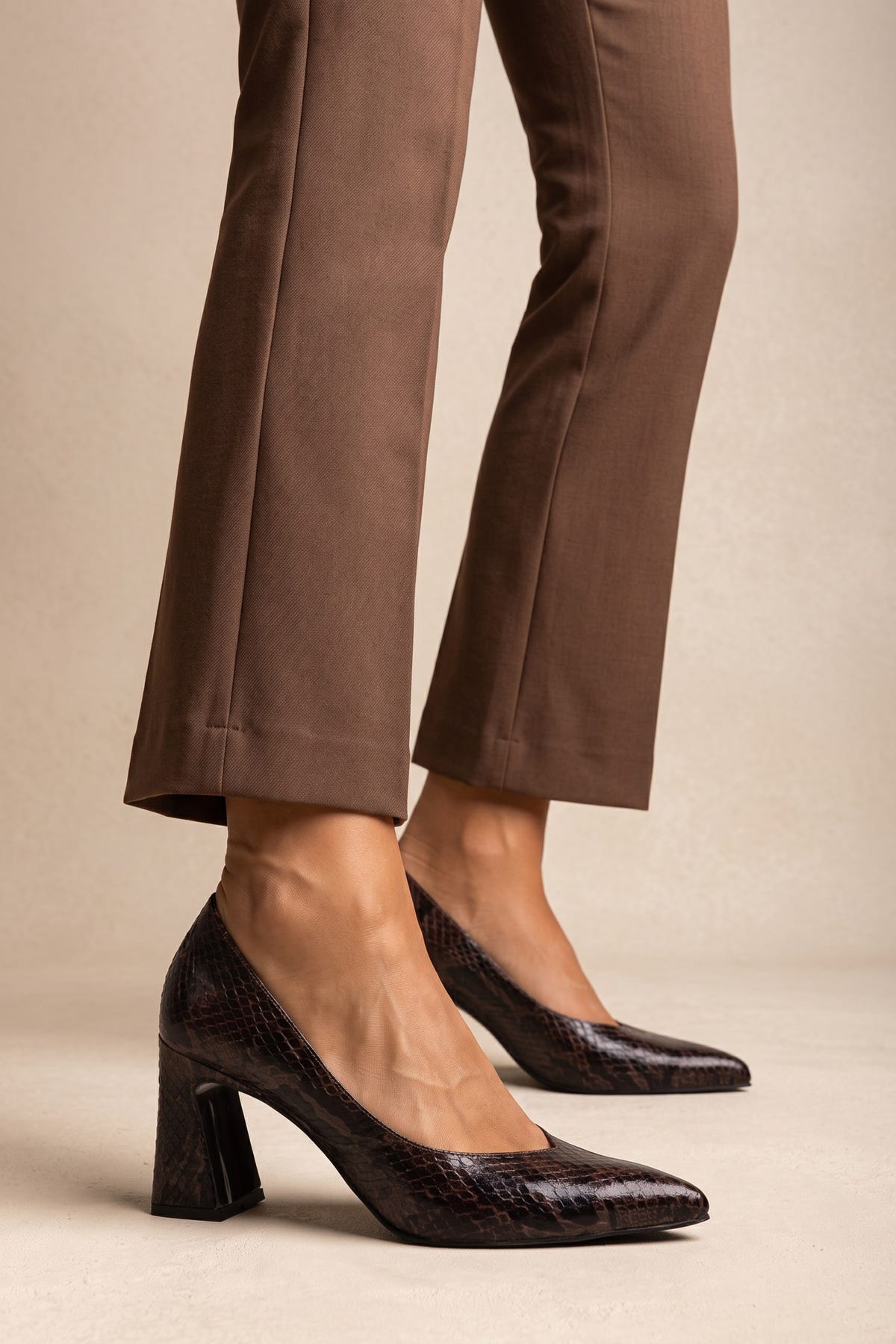 Model wearing brown trousers and brown snake-print pumps, legs cropped to show shoes in side view