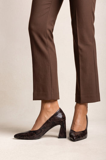 Model in brown trousers wearing brown snake-print pointed-toe pumps standing full length