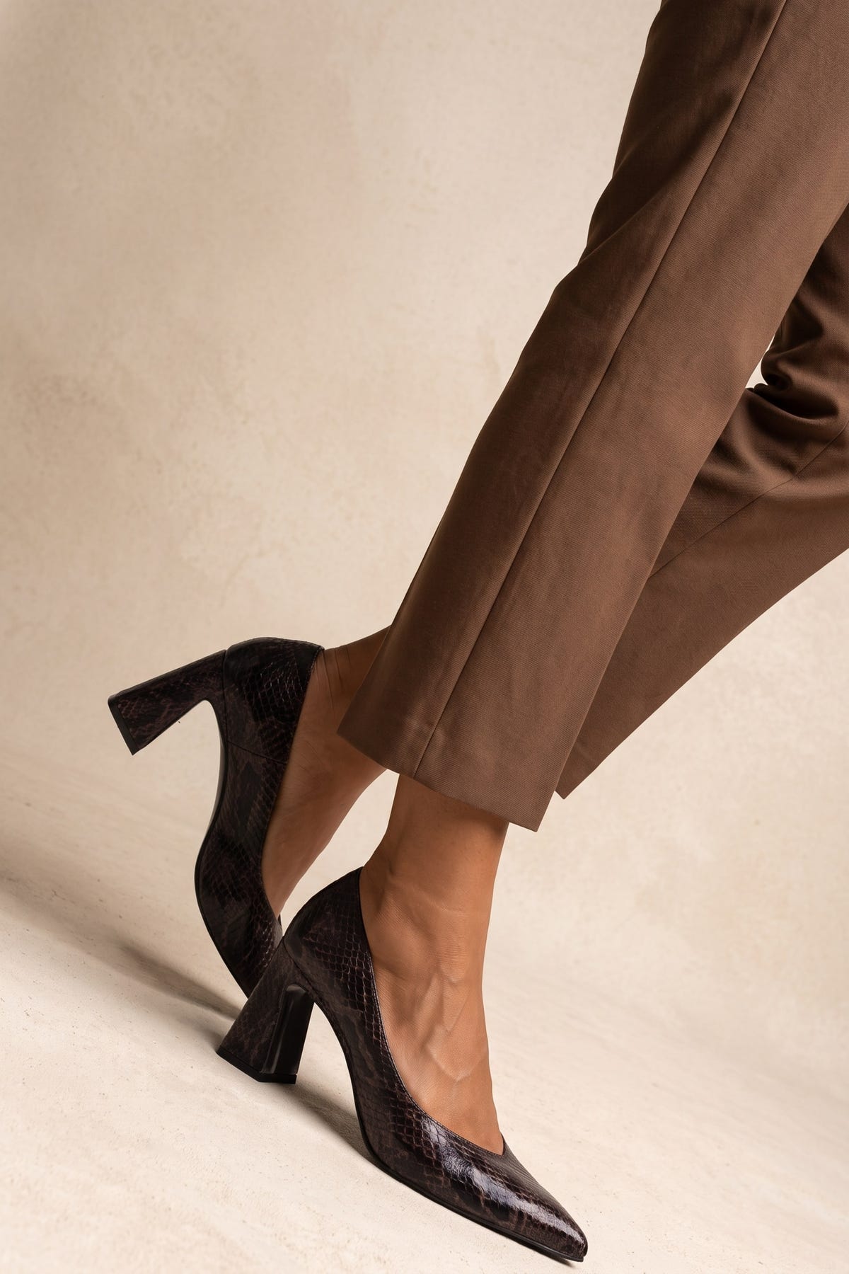 Model in brown trousers stepping forward in brown snake-print pumps showing flared block heel