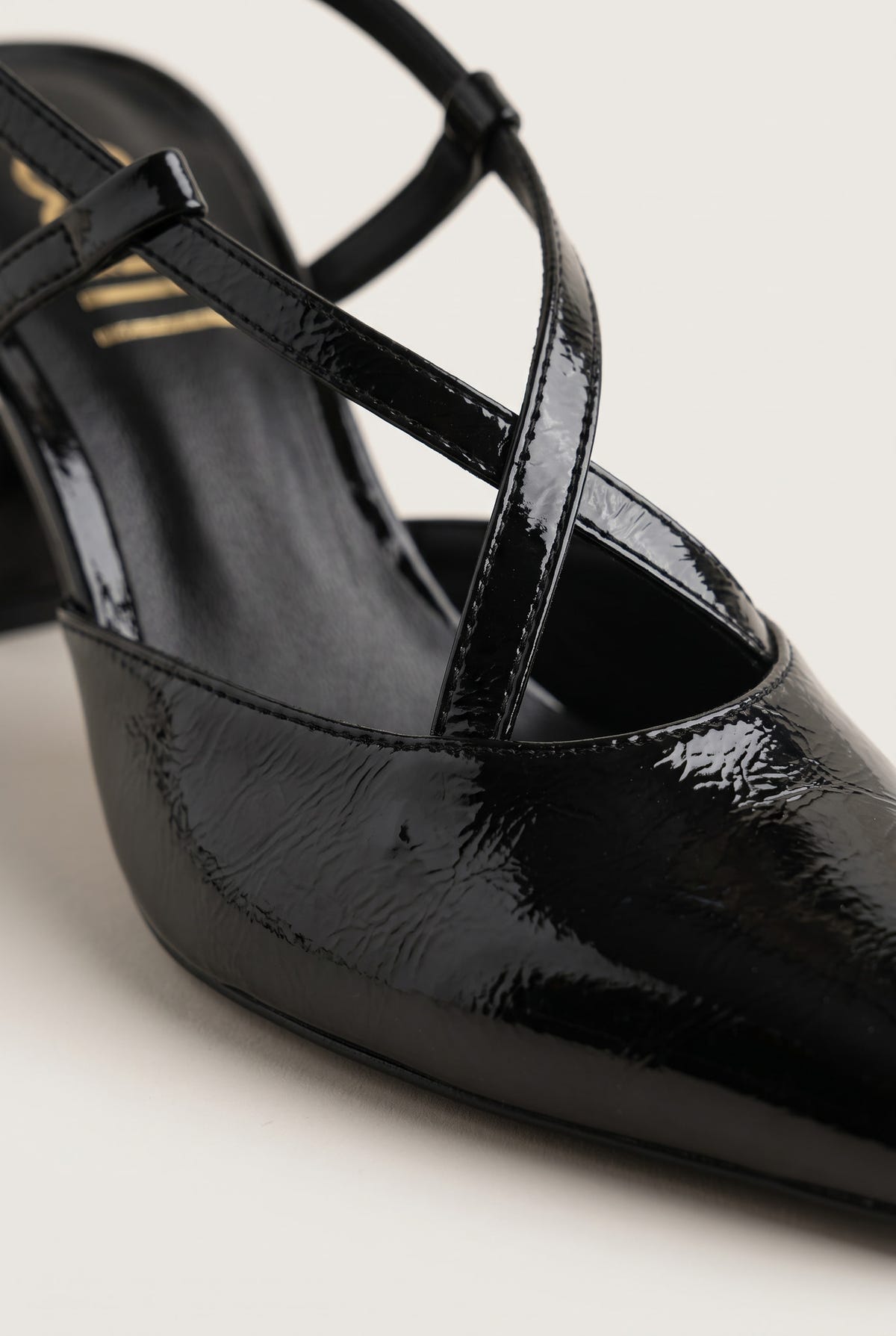 Close-up of glossy black patent pointed toe and crossed strap on a block heel slingback