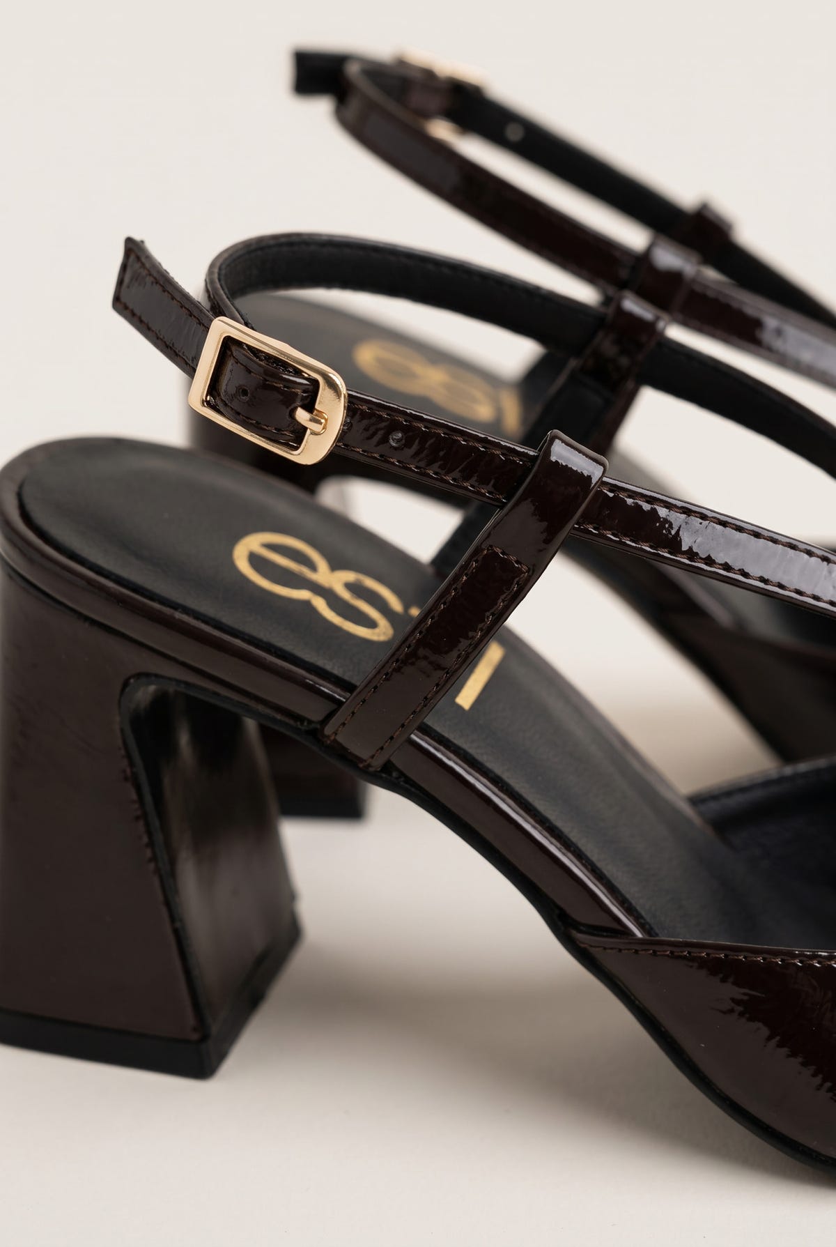 Close-up of a gold buckle on the glossy brown patent ankle strap of a slingback pump with a block heel and cushioned insole