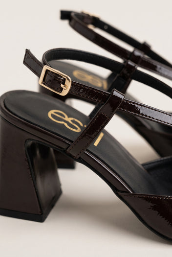 Close-up of a gold buckle on the glossy brown patent ankle strap of a slingback pump with a block heel and cushioned insole