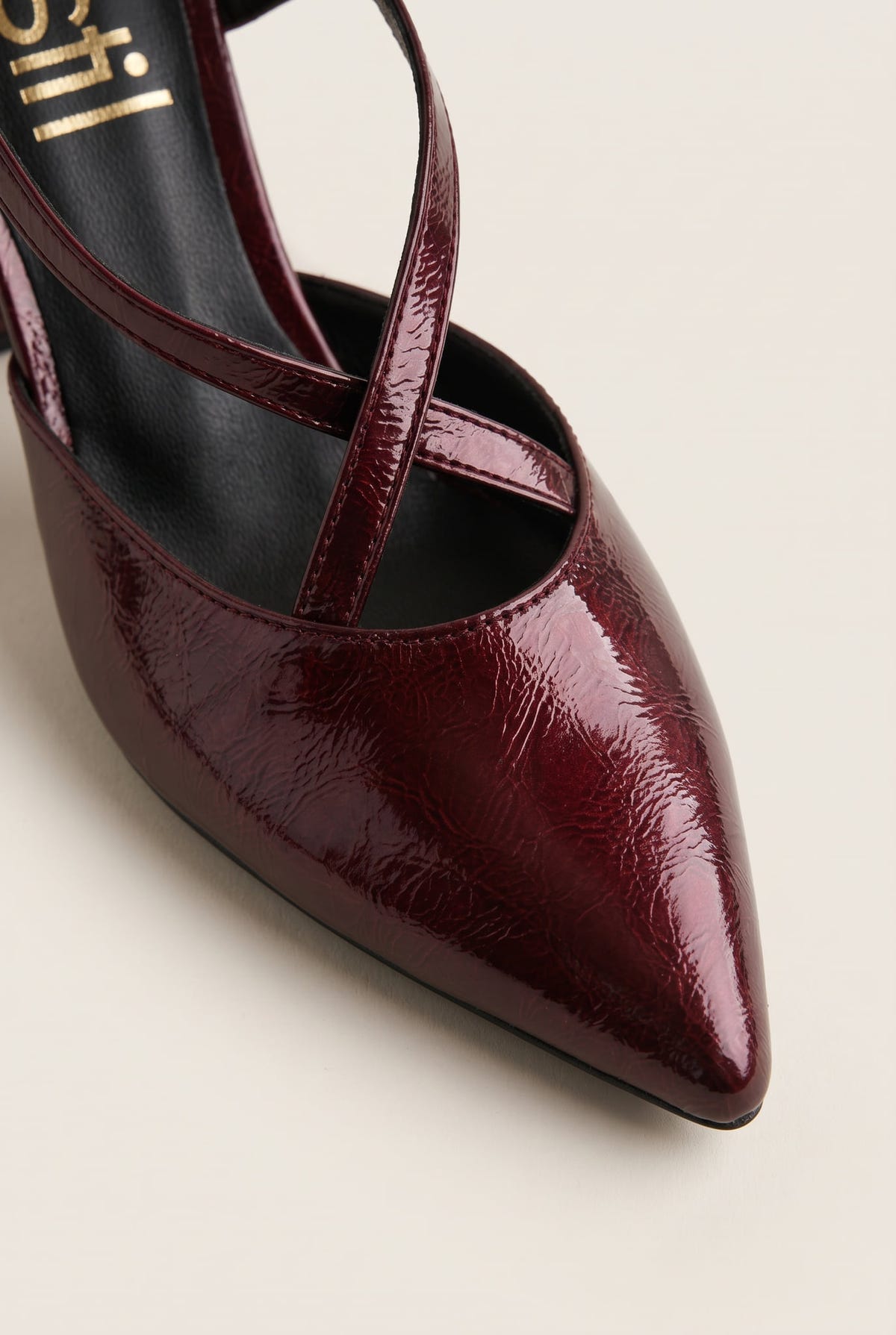 Close-up of glossy bordeaux patent pointed toe and strap curving over a block heel pump