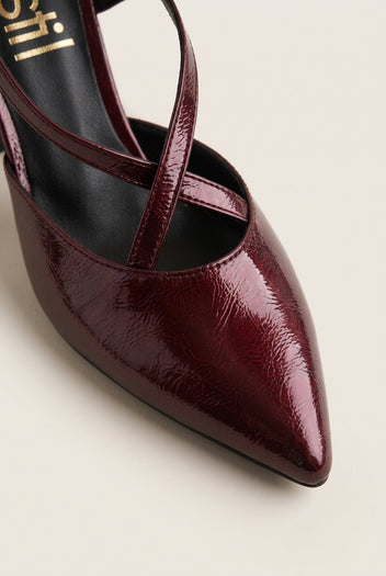 Close-up of glossy bordeaux patent pointed toe and strap curving over a block heel pump