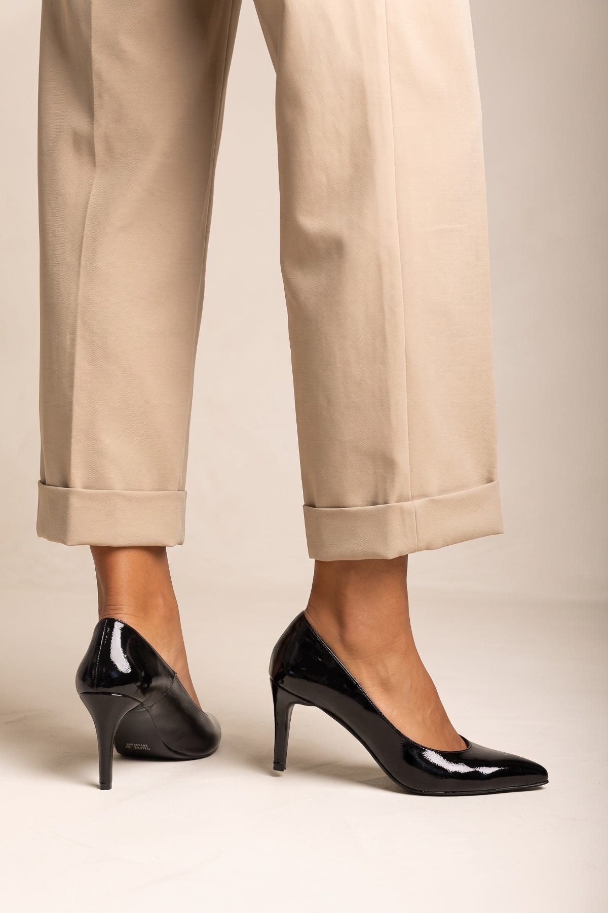 Black patent pointed toe stiletto pump, worn by model in beige trousers, side view