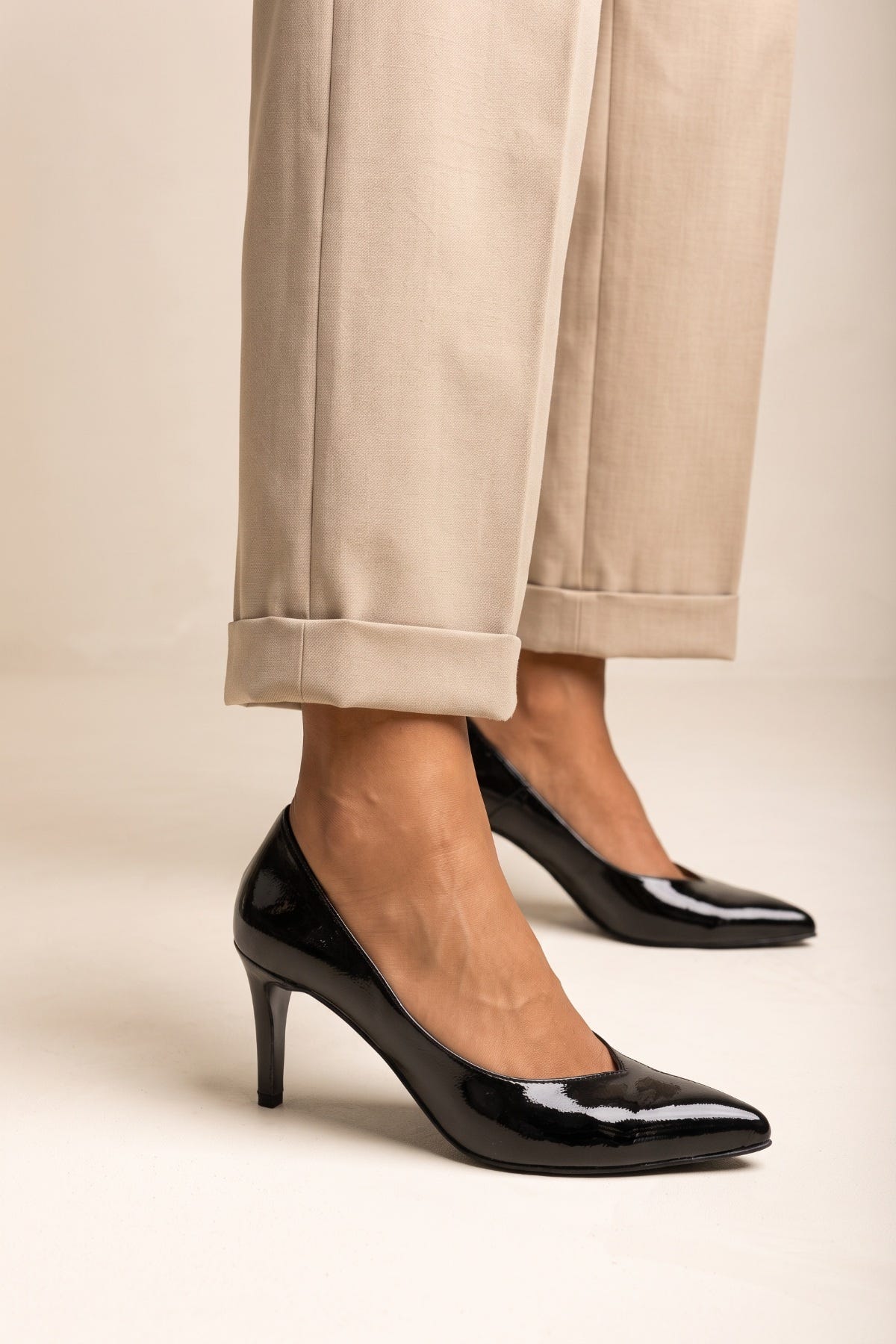Black patent pointed toe stiletto pump, close side view on model in beige cuffed trousers