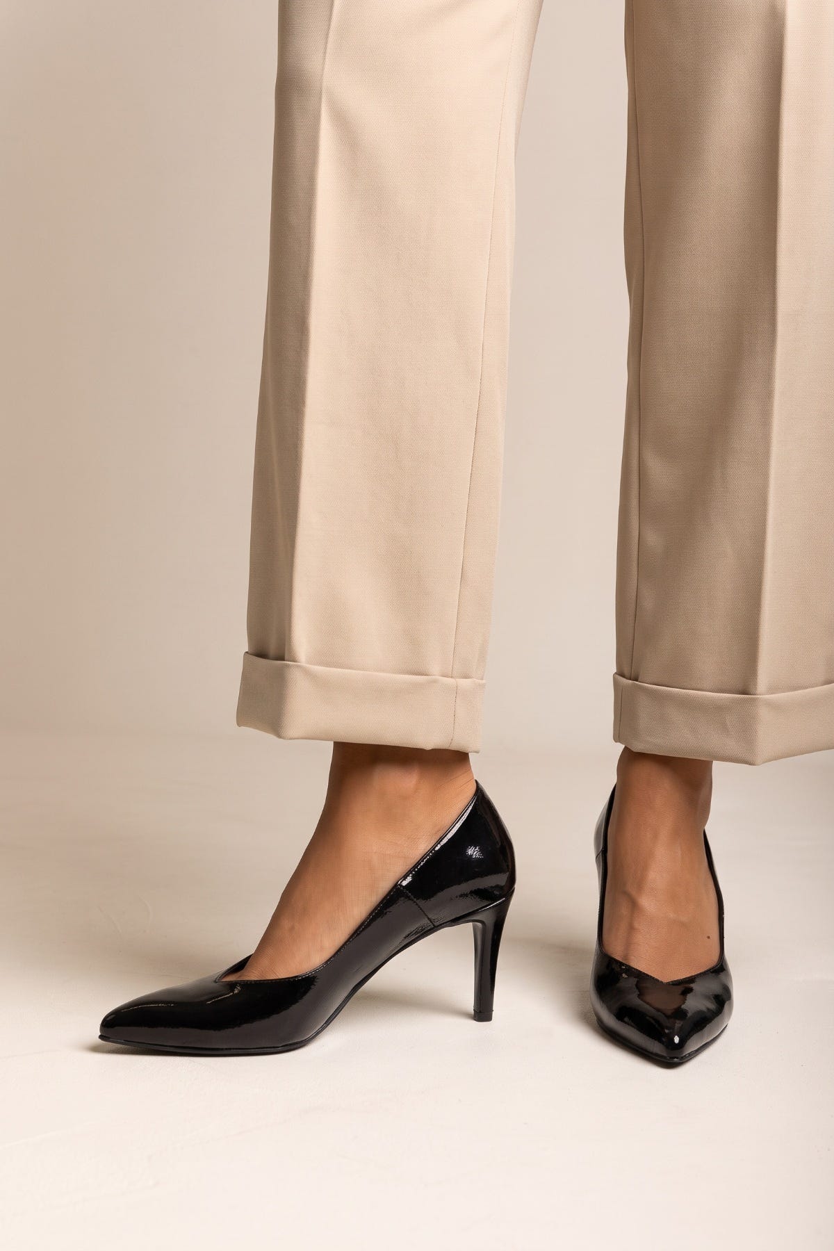 Black patent pointed toe stiletto pump with slim heel, front view of the pair with beige trousers