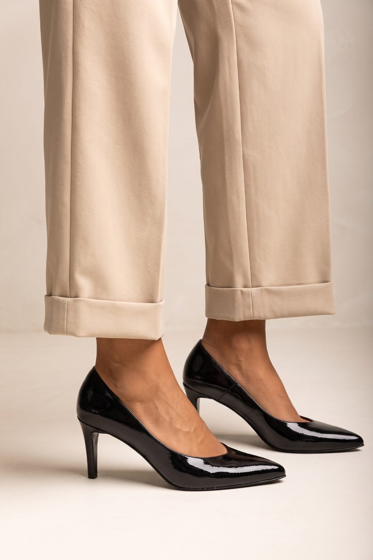Black patent pointed toe stiletto pump with high heel, pair worn with beige trousers