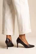 Model wearing brown snake print stiletto pumps with pointed toes and cream cuffed trousers