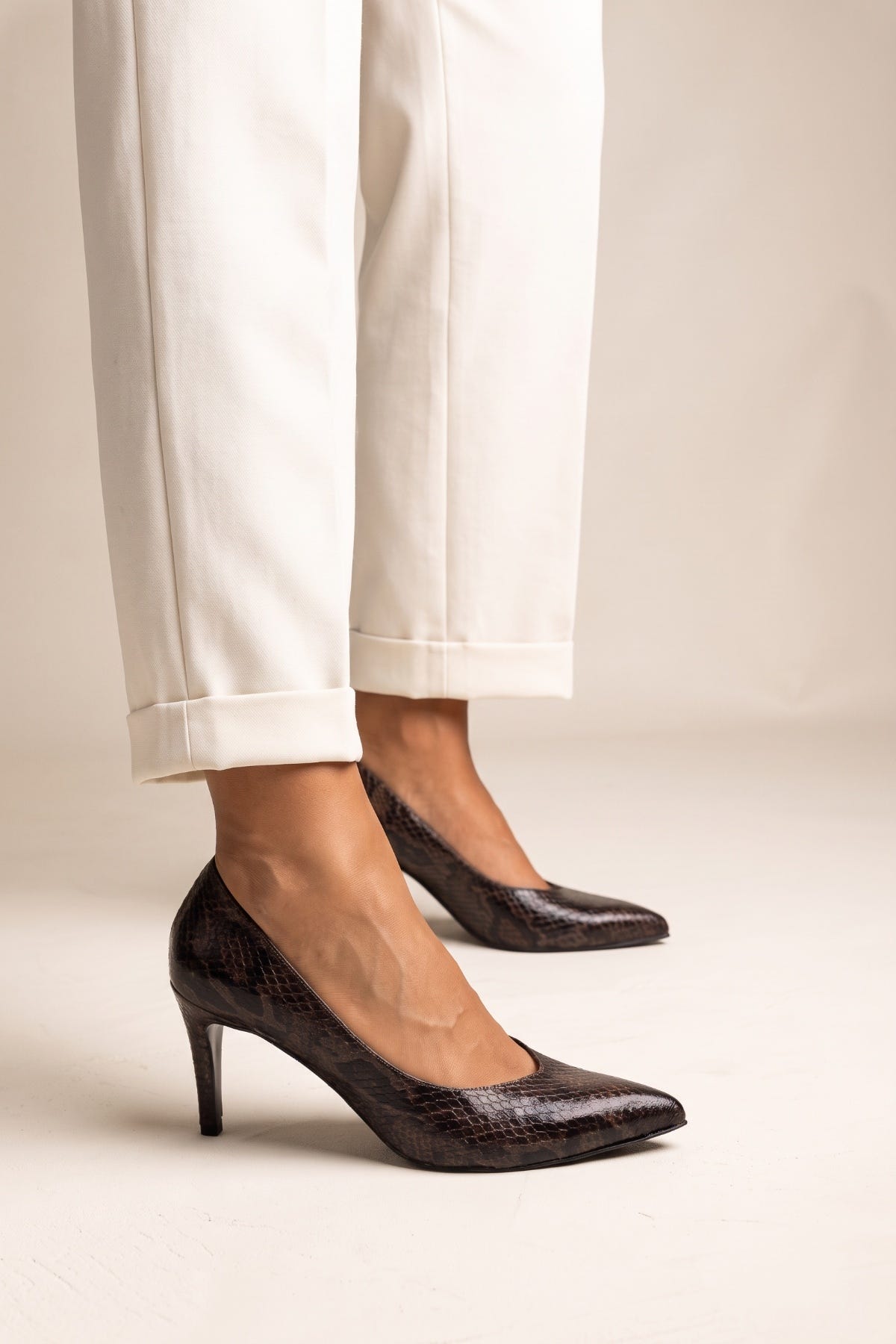 Front view of model in brown snake print stiletto pumps with pointed toes and cream trousers
