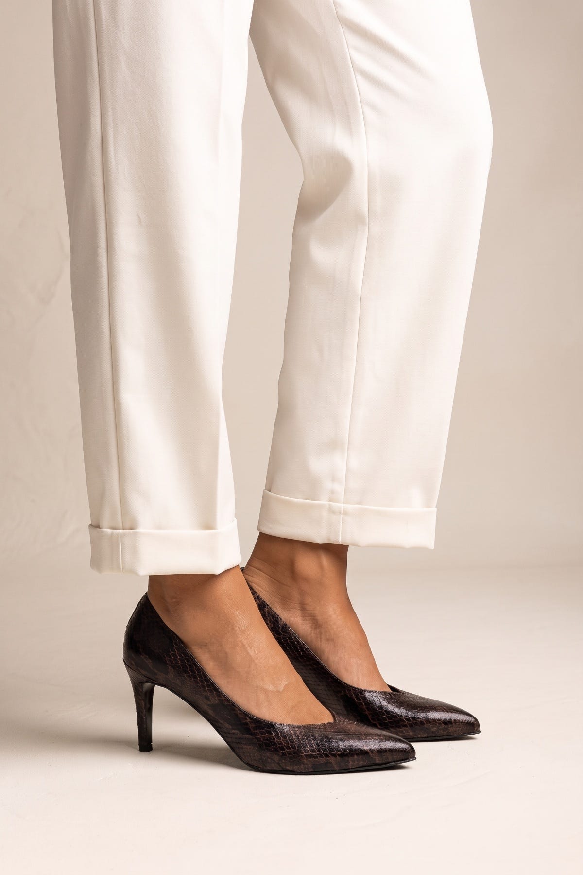 Model stepping in brown snake print stiletto pumps with pointed toes and white cuffed trousers