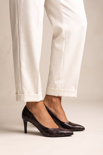 Model stepping in brown snake print stiletto pumps with pointed toes and white cuffed trousers