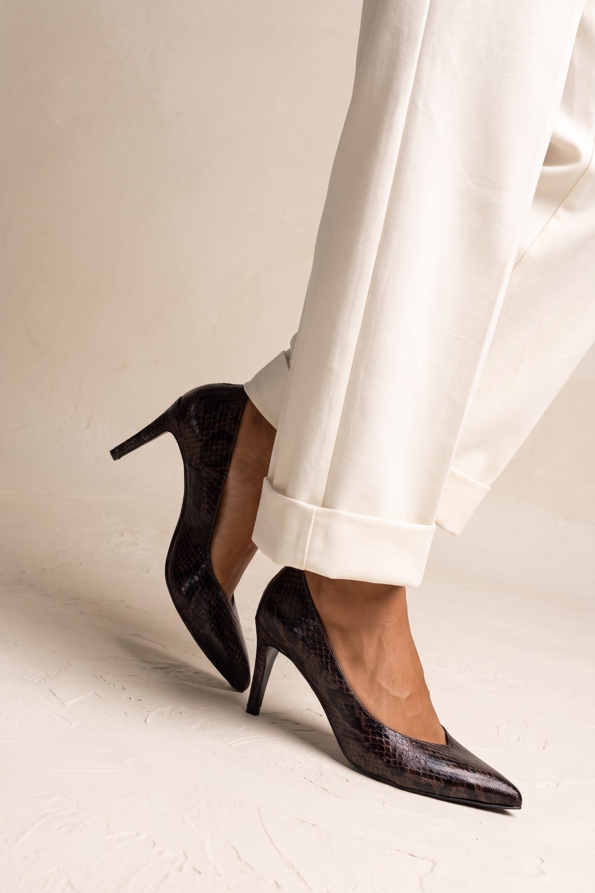 Model in brown snake print stiletto pumps seen from the side with a slim heel and cuffed trousers
