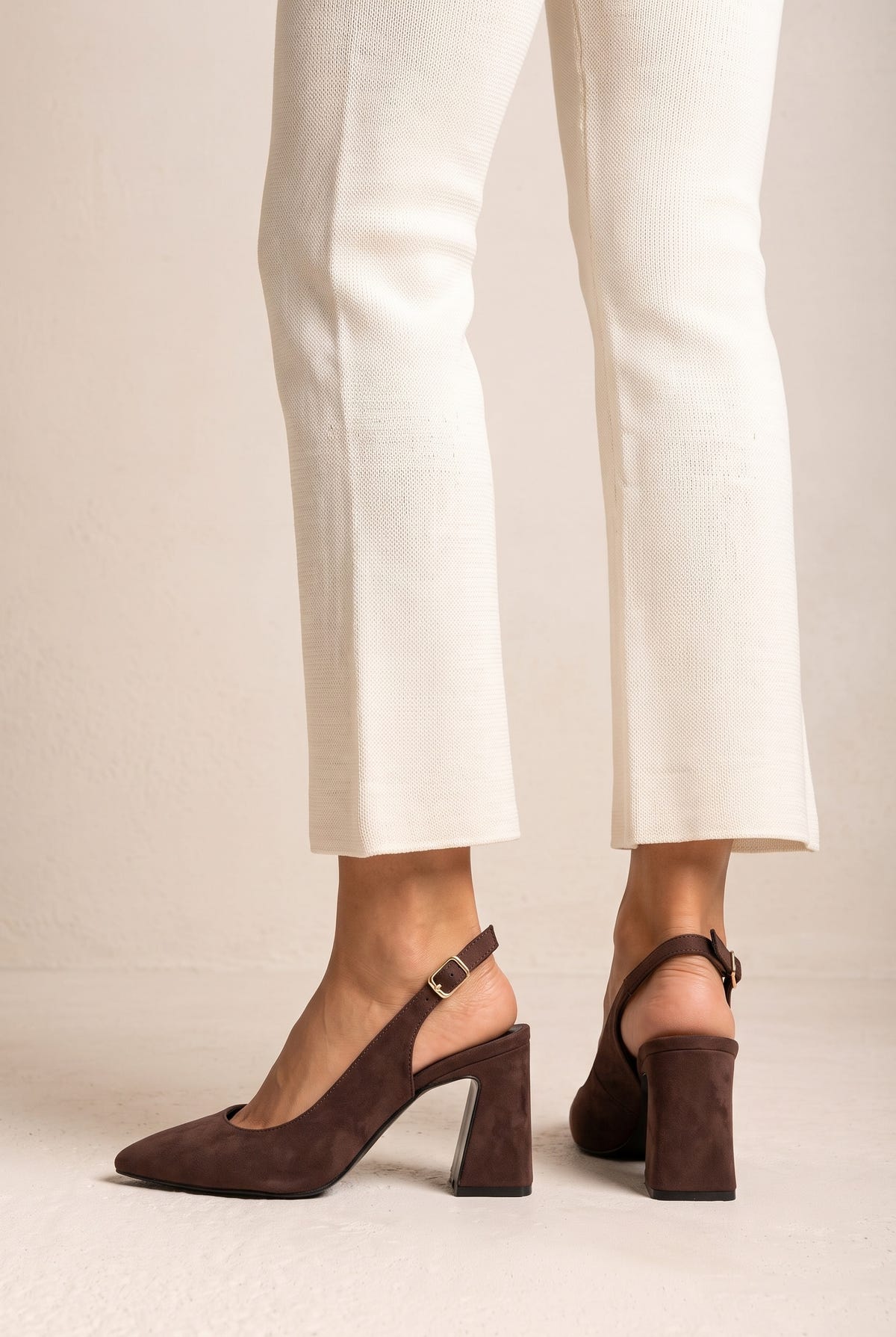 Model wearing brown suede slingback pumps with cream trousers, legs seen from mid-calf down with the buckled straps visible