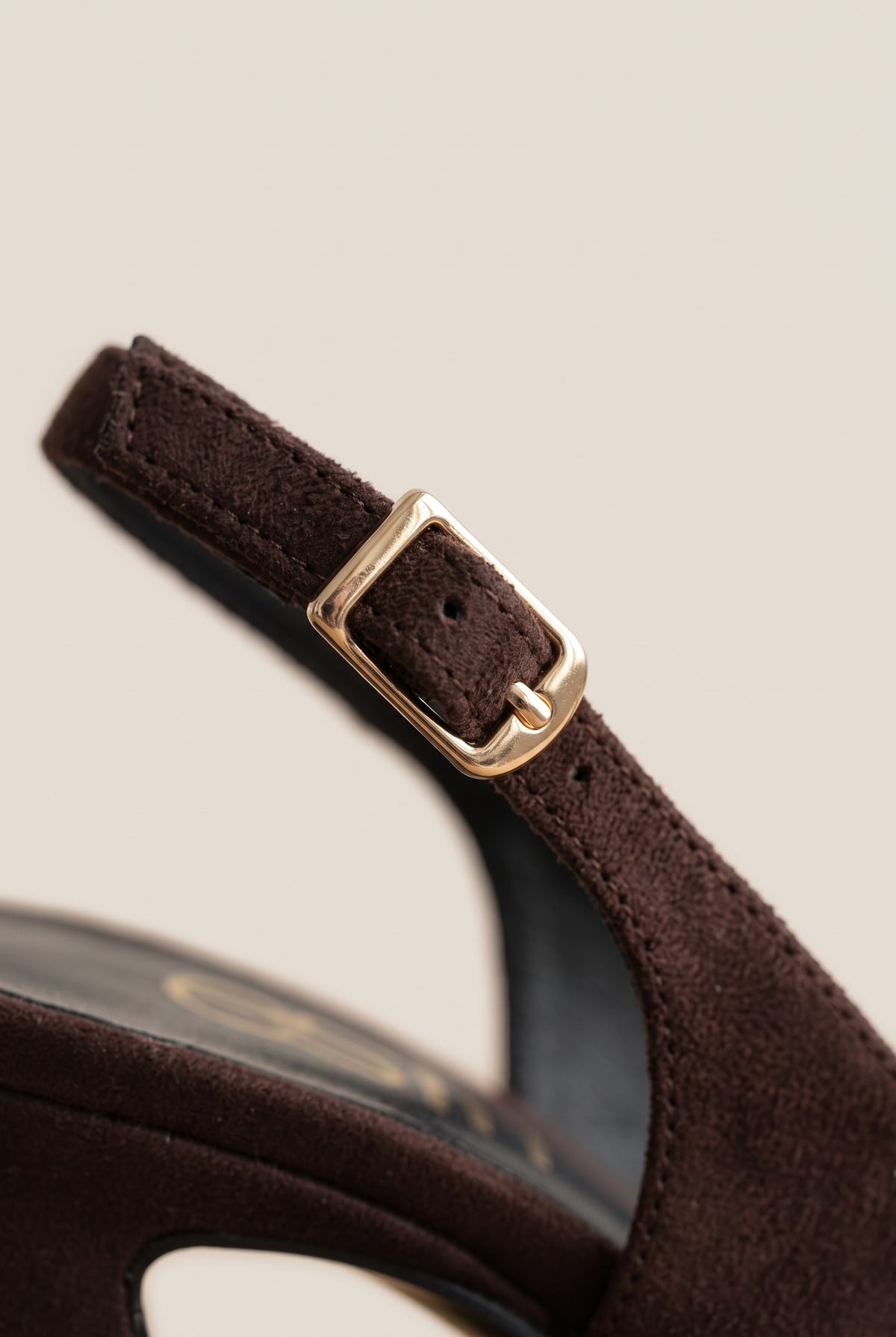 Close-up of a brown suede slingback strap with a gold buckle beside the block heel of the shoe