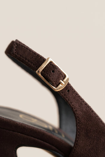 Close-up of a brown suede slingback strap with a gold buckle beside the block heel of the shoe