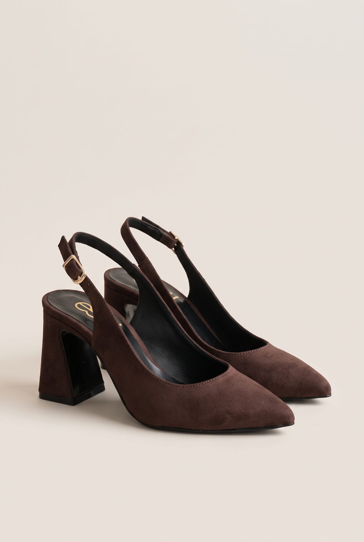 Pair of brown suede slingback pumps with pointed toes and block heels, tilted on a beige wall to show both shoes
