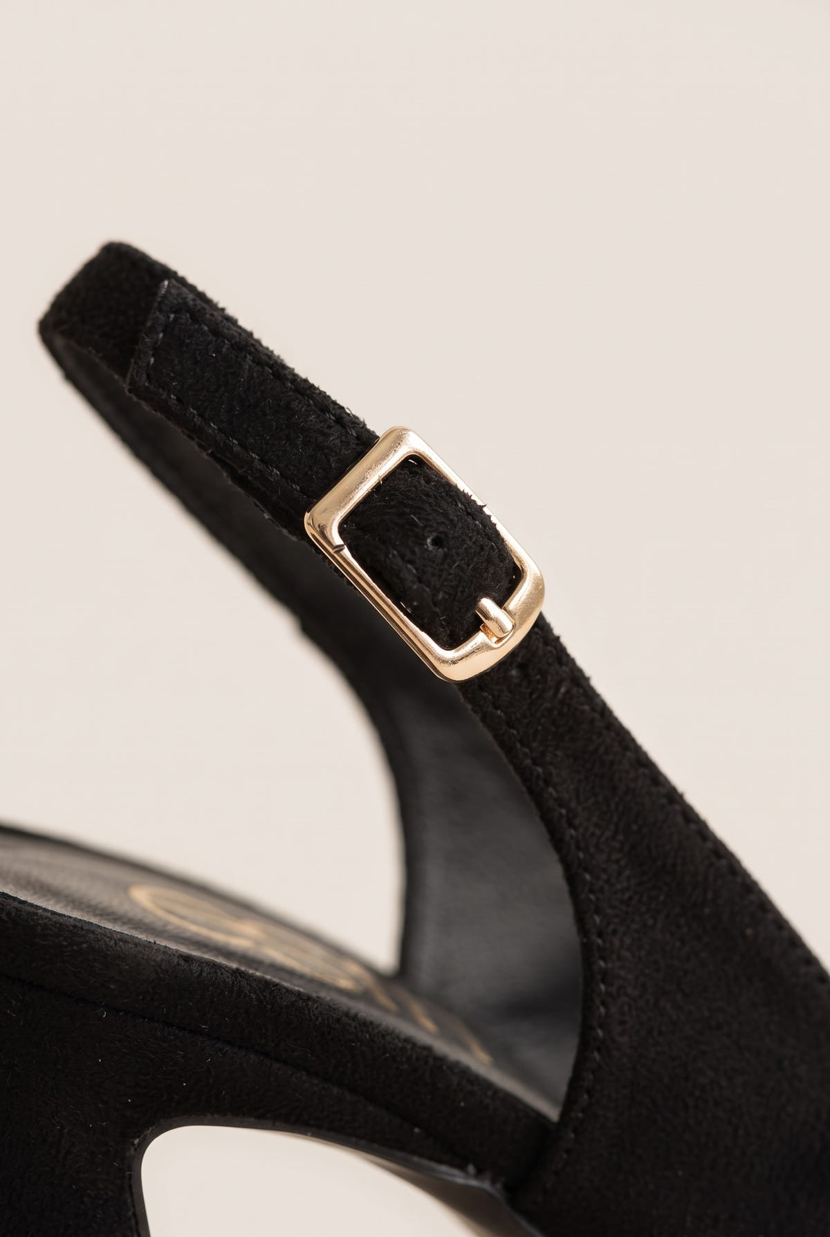 Close-up of a black suede slingback strap with a gold buckle set above the heel of the shoe