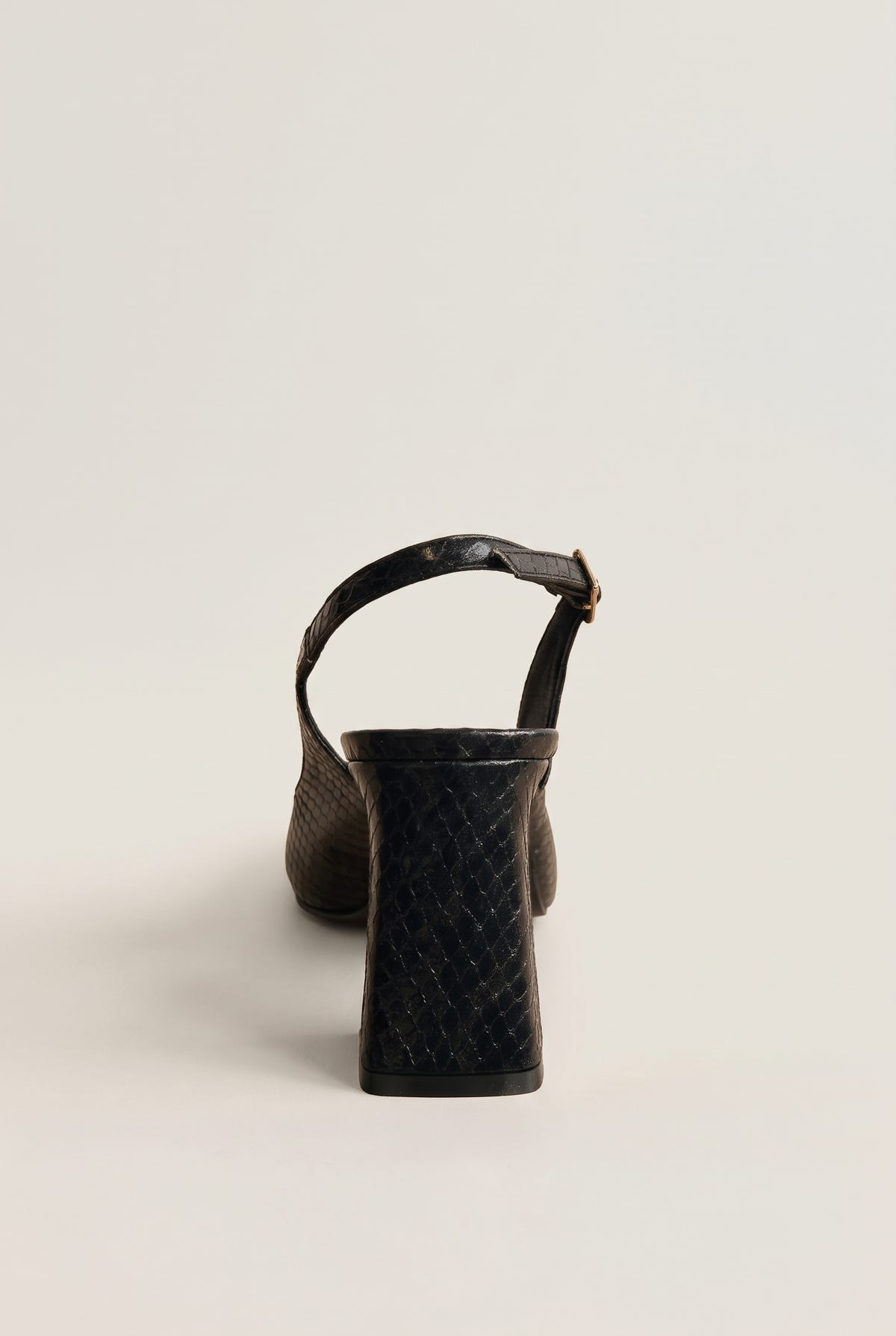 Back view of a black snake-embossed slingback pump showing its block heel and slim ankle strap with a gold buckle