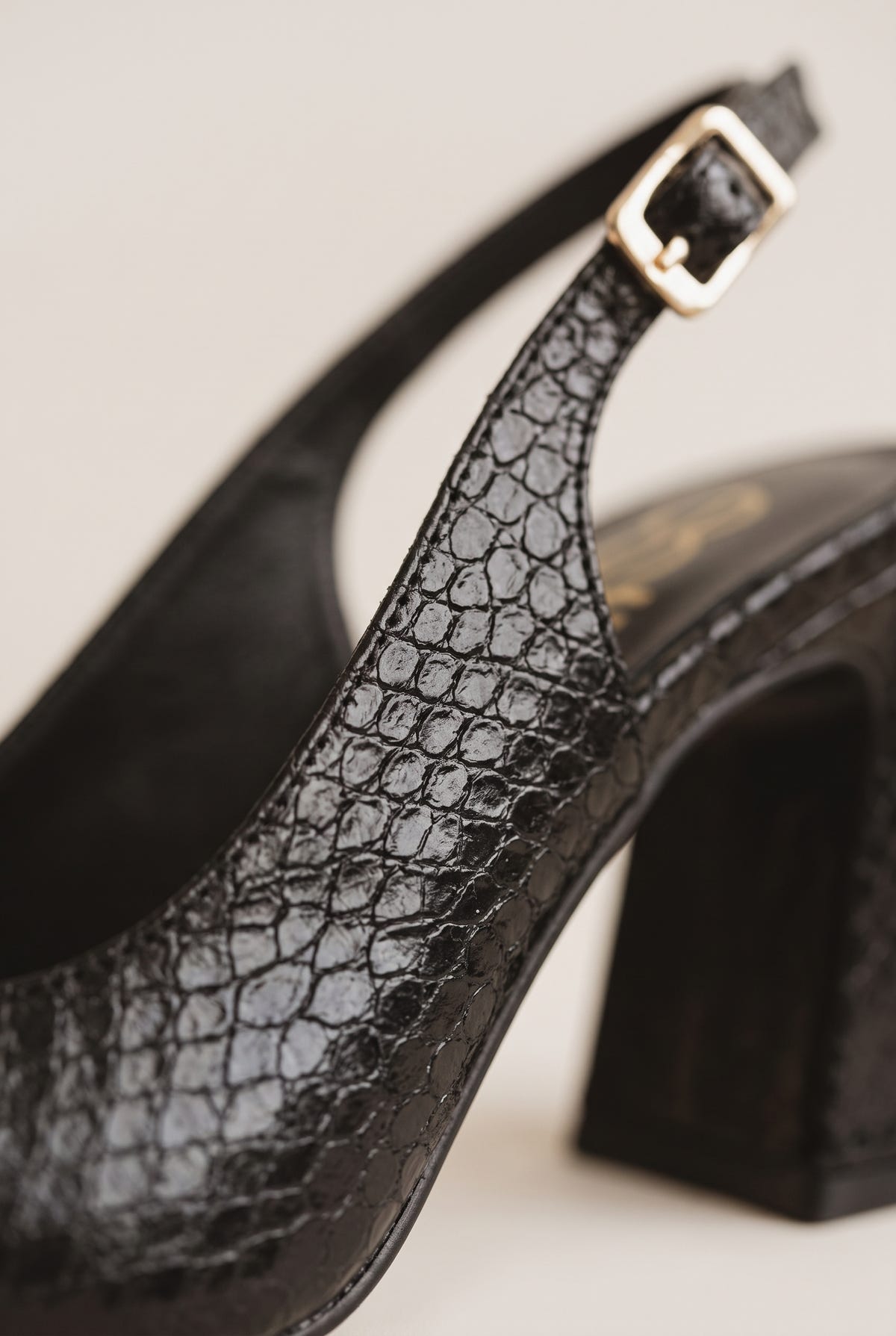 Close-up of black snake-embossed slingback pump showing a gold buckle strap, sculpted block heel and glossy pointed toe edge