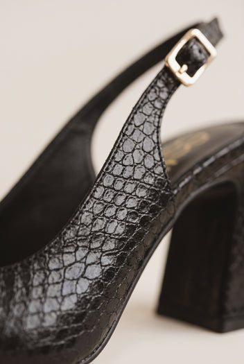 Close-up of black snake-embossed slingback pump showing a gold buckle strap, sculpted block heel and glossy pointed toe edge