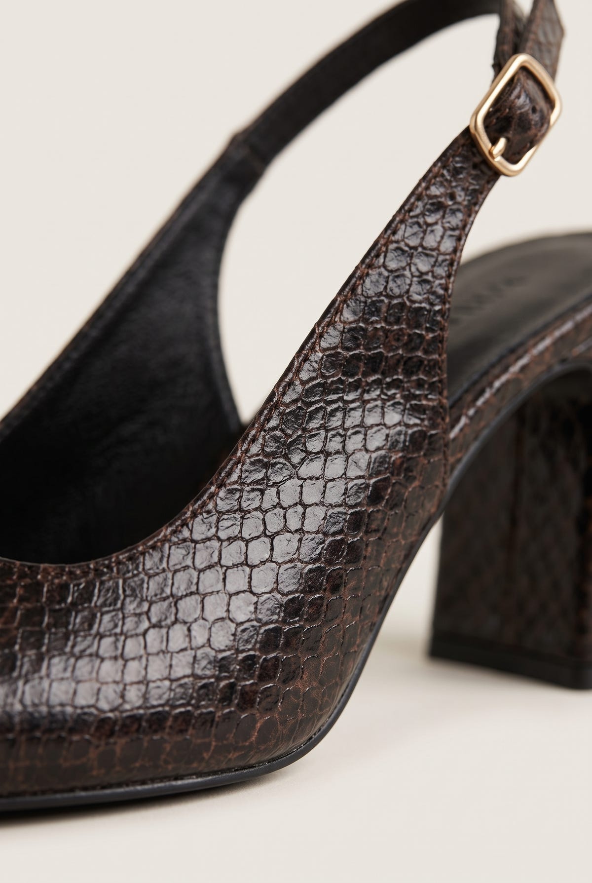 Close-up of brown snake-embossed leather on a slingback pump with a gold buckle strap and sculpted block heel