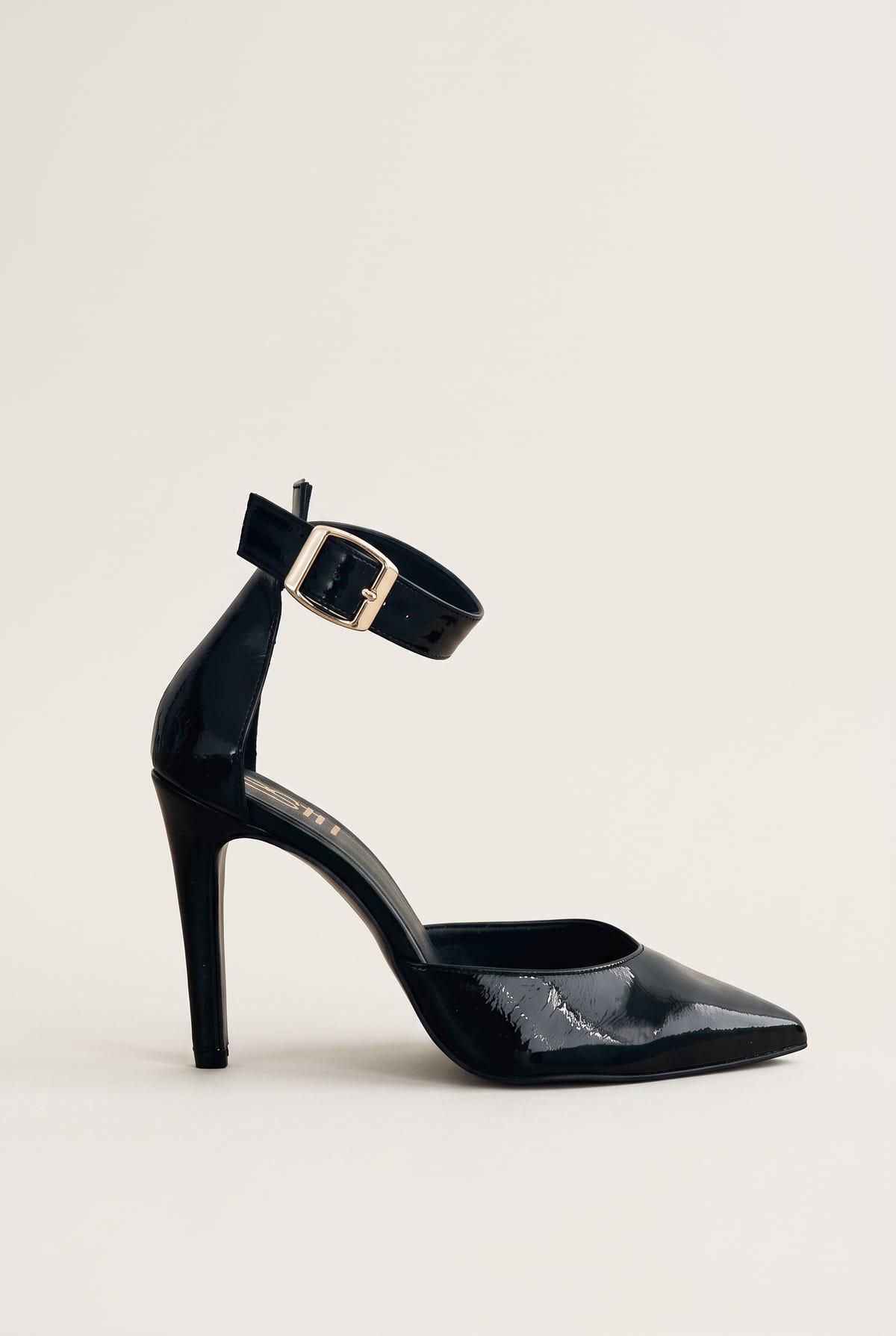 Side view of a black patent stiletto pump with a pointed toe, slim high heel and gold buckled ankle strap