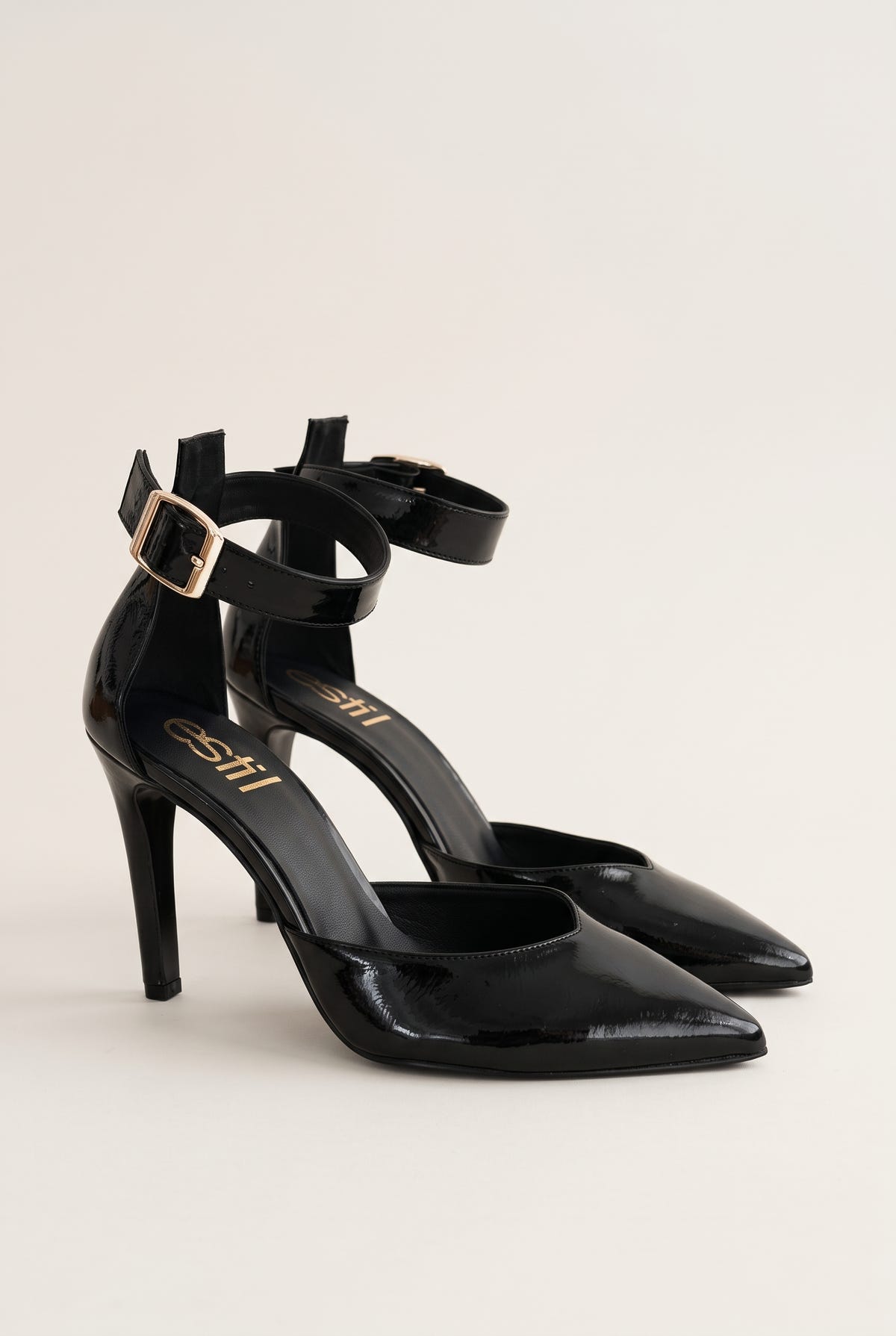 Pair of black patent pointed-toe stiletto pumps with double ankle straps and gold buckles, viewed from the front and side