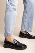 Model wearing black patent chunky loafers with snake-embossed penny strap and light wash denim jeans