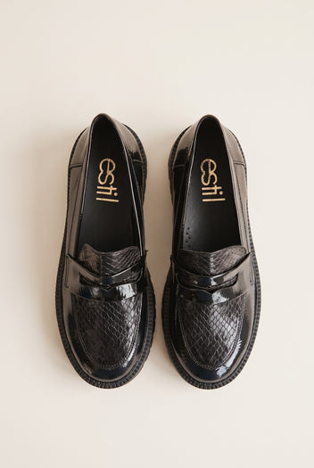 Top view of black patent chunky loafers with snake-embossed vamp and penny strap placed side by side