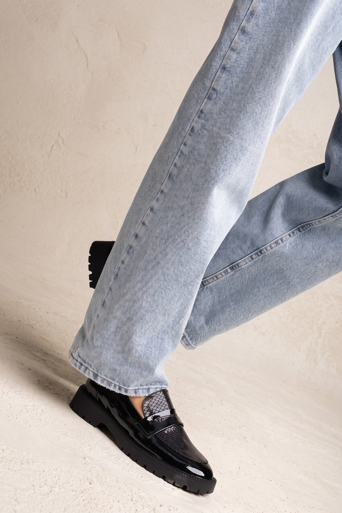 Model stepping in black patent chunky loafer with light wash jeans, side view of lower legs