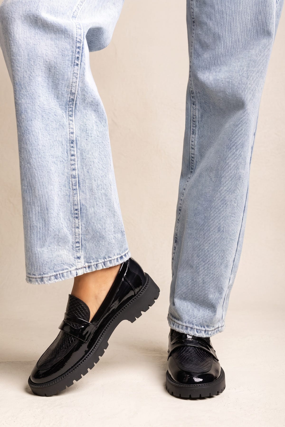 Model wearing black patent chunky loafers with snake-embossed strap and light wash wide-leg jeans