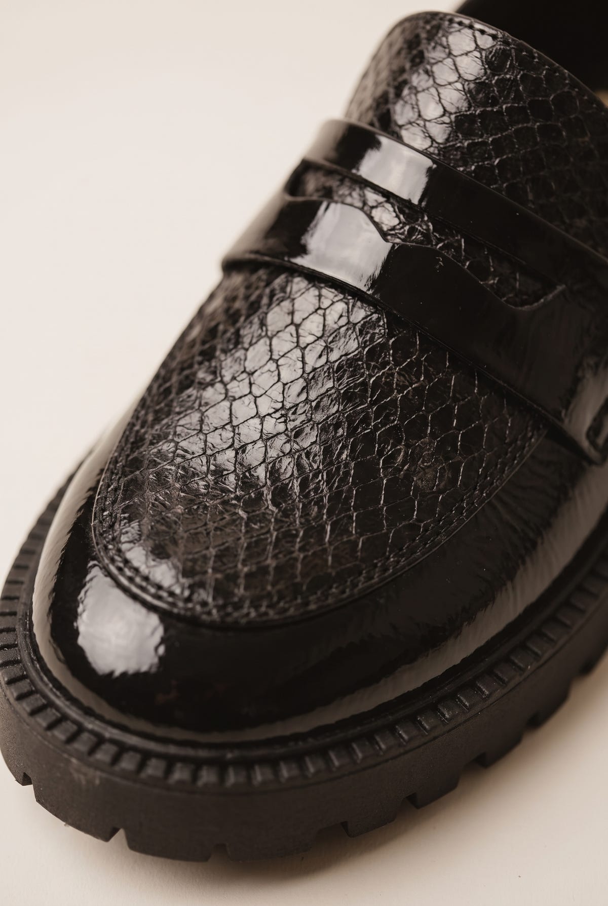 Close-up of black patent leather loafer vamp with snake-embossed texture and lug sole edge