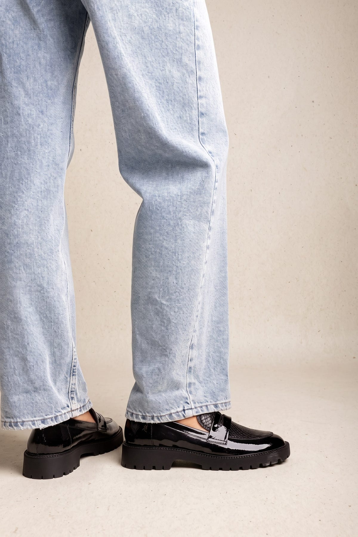 Model wearing black patent chunky loafers with penny strap and light wash straight-leg jeans, front view