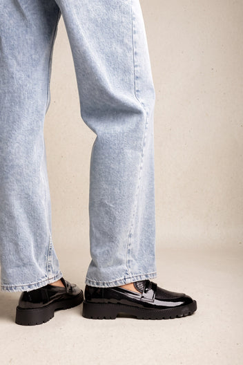 Model wearing black patent chunky loafers with penny strap and light wash straight-leg jeans, front view
