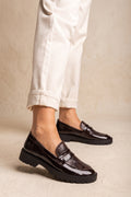 Model wearing brown patent snake-embossed chunky loafers with cream rolled-cuff trousers, lower legs visible