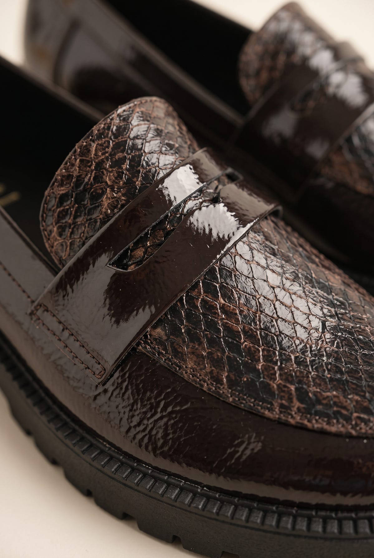 Close-up of brown patent snake-embossed loafer vamp and penny strap over a dark lug sole