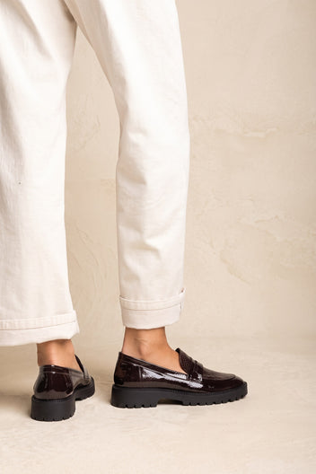 Model in cream trousers with brown patent snake-embossed chunky loafers, both feet side by side